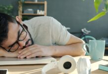 ‘만성피로, 생활 속 작은 변화로 극복할 수 있을까?’ Man sleeping at desk with headphones and coffee.
