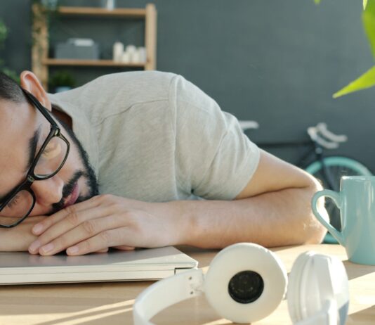 ‘만성피로, 생활 속 작은 변화로 극복할 수 있을까?’ Man sleeping at desk with headphones and coffee.