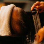 “두피부터 건강하게, 요즘 뜨는 헤어케어 루틴” a man getting his hair washed in a sink
